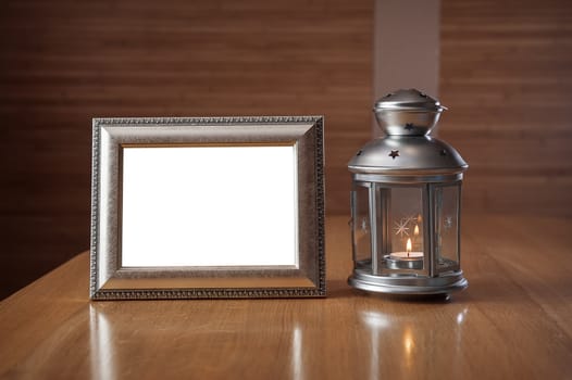 old photo frame on the wooden table against the background of a lantern with a candle