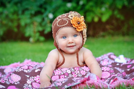A cute little baby is looking into the camera and is wearing a brown hat. The baby could be a boy or girl and has blue eyes. use it for a parenting or love concept. 