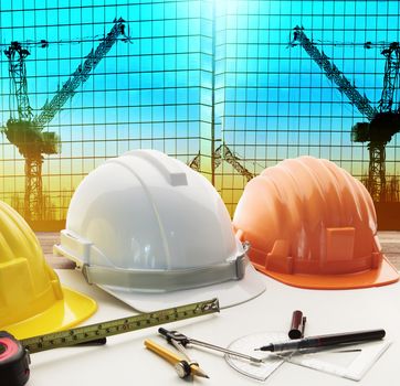 safety helmet on architect ,engineer working table with modern building and crane construction background use for construction business and civil engineering ,real estate topic