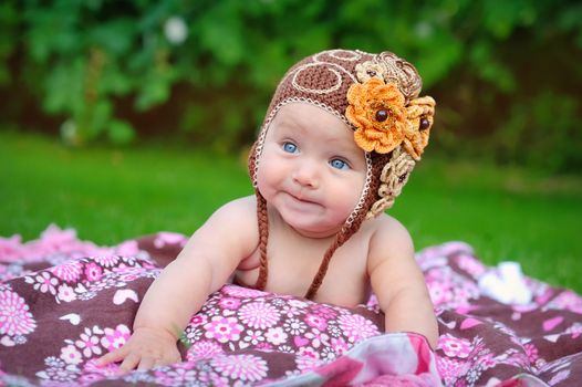 Cute baby crawling outdoors in brown knitted cap