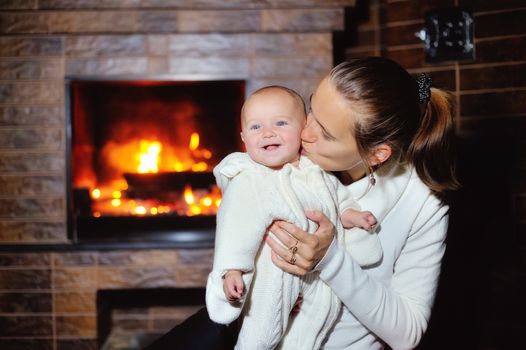 Mom kissing baby by the fireplace at home