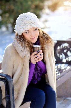 happiness, winter holidays, christmas, beverages and people concept - smiling young woman in white hat and mittens with coffee cup over shopping center background 