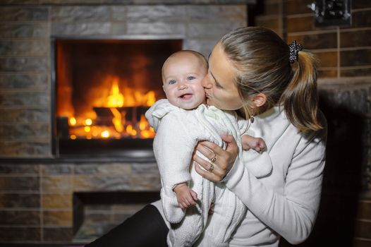 Mom kissing baby by the fireplace at home