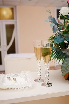 two glasses of champagne and pillow with rings on the table for wedding ceremony.