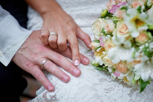 hands of the bride and groom with rings and wedding bouquet.