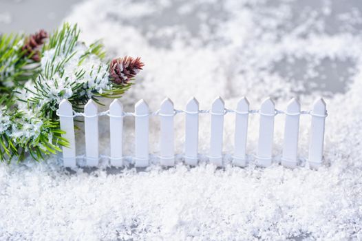 snow-covered spruce twigs and toy white fence. Christmas installation.