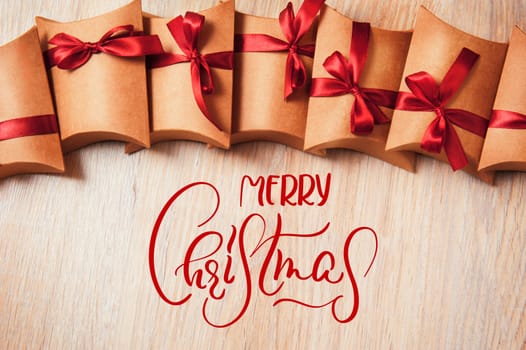 Gift box wrapped in kraft paper with ribbon bow and text Merry Christmas. Calligraphy lettering.
