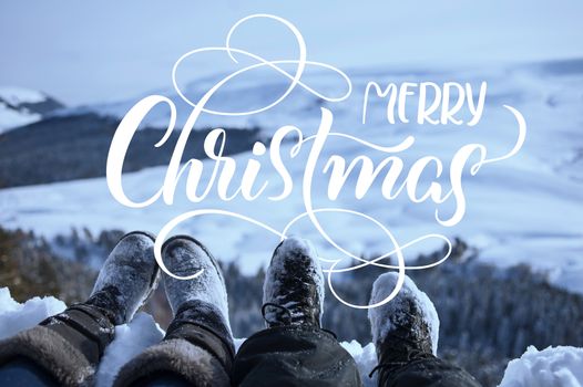 snow-covered feet of two hikers on a winter landscape with text Merry Christmas. Calligraphy lettering.