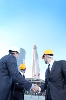 Architects wearing helmets shaking hands at skyscrapers background