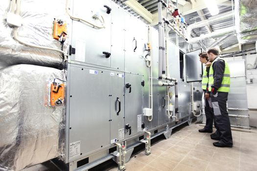 Two workers check switchboards at factory auxiliary room