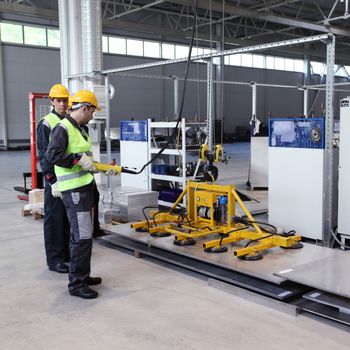 Workers near metal sheet lifting device at factory