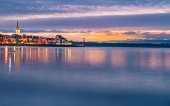 Enchanting landscape with a colorful sky reflected in the water of the Bodensee lake, as the sun is coming up, over Friedrichshafen town, Germany.