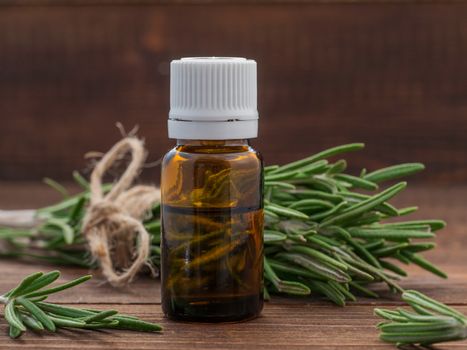 Rosemary essential oil in dark glass bottle and fresh rosemary on dark wooden background with copy space