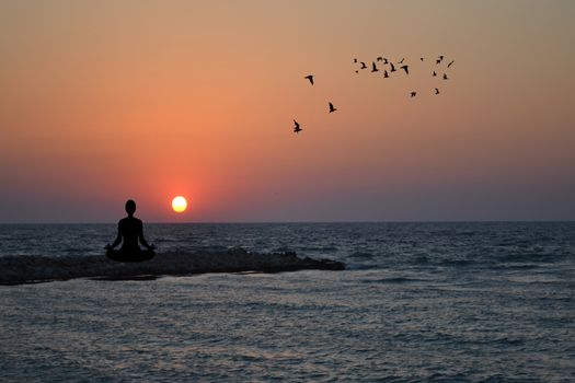 Silhouette of woman practising yoga and meditating on sunrise