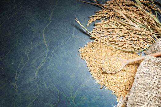 Brown rice uncooked in a bag with a pile of brown rice with over a full spoonful of rice and spike rice on table background.