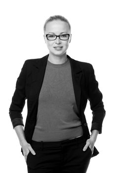 Black and white portrait of beautiful smart young businesswoman in business attire wearin black eyeglasses, standing with arms in pockets against white background.