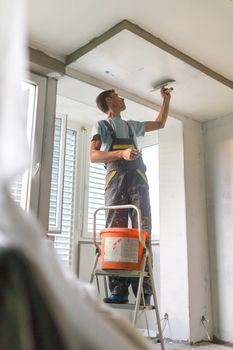 Construction worker wearing worker overall with wall plastering tools renovating apartment house. Plasterer renovating indoor walls and ceilings with float and plaster. Construction finishing works.