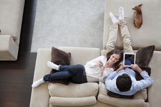 Couple using digital tablet at home sitting on sofa, top view