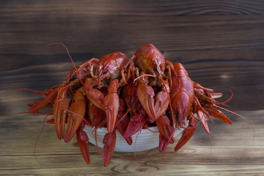 Plate of red boiled crayfishes with claws on wooden background