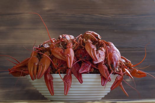 Plate of red boiled crayfishes with claws on wooden background
