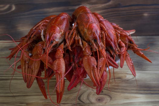 Plate of red boiled crayfishes with claws on wooden background