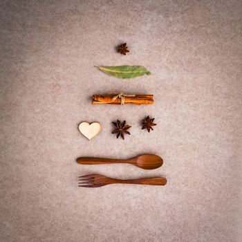 Background for christmas menu . Shape of Christmas tree from wooden spoon ,fork ,cinnamon ,star anise ,wooden heart and bay leaves set up on brown paper board Concept for christmas  day menu .