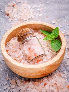 Closeup Himalayan pink salt in wooden bowl and bottle  with peppermint leaves on stone background. Himalayan salt commonly used in cooking and for bath products such as bath salts.