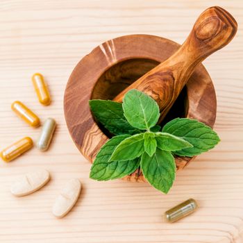Fresh peppermint leaves in olive wood mortar and capsule of herbal medicine . Alternative health care concept setup on wooden background.