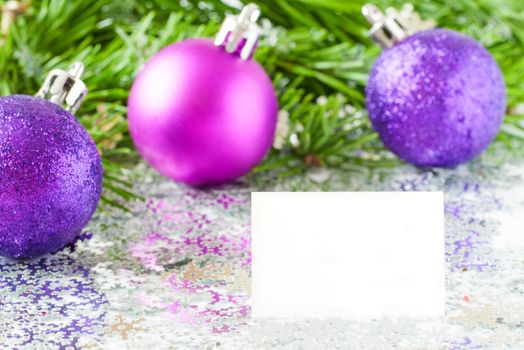 Fir tree branch and Christmas toys bauble and snow flares confetti with white card for your text. Horizontal orientation with copy space.