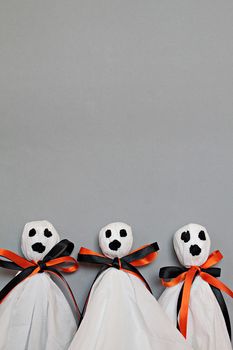 Halloween concept background : Three halloween ghosts DIY made from white tissue paper, black and orange ribbon on gray background