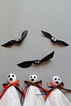 Halloween concept background : Three halloween ghosts DIY made from white tissue paper, black and orange ribbon and three bats DIY made form black ribbon on gray background