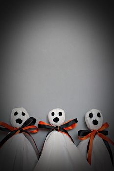 Halloween concept background : Three halloween ghosts DIY made from white tissue paper, black and orange ribbon on gray background