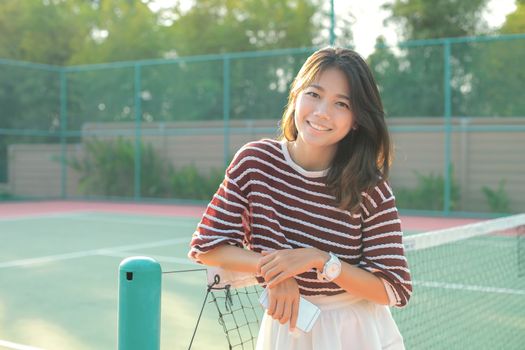 portrait of beautiful young asian woman wearing white clothes skirt in tennis course with happy face 