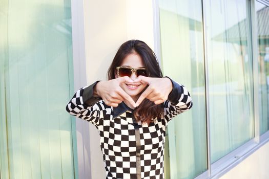 portrait of young beautiful hipster woman wearing sun glasses making heart symbol by finger hand