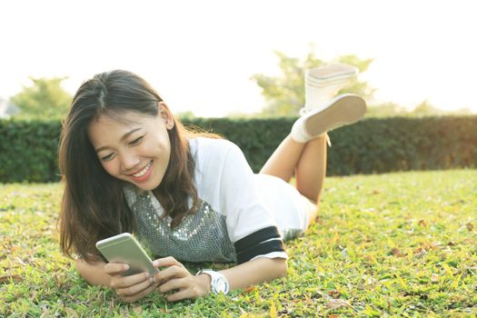 portrait of beautiful young woman lying and playing and watching to smart phone screen in home garden field with happy face 