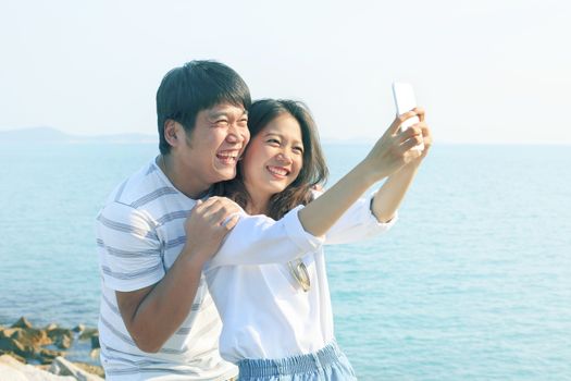 young man and woman take a photo by smart phone at sea side use for new people life style and technology activities 