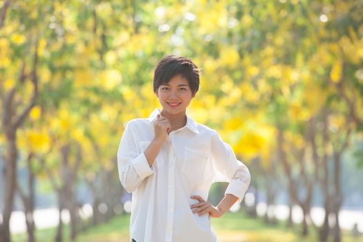 portrait of young beautiful asian woman with white shirt standing and smiling face in blur yellow flowers blooming background use for people and summer activities on location