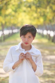 portrait of beautiful young asian woman wearing white shirts standing in blooming yellow flowers park and looking to camera with eyes contact 