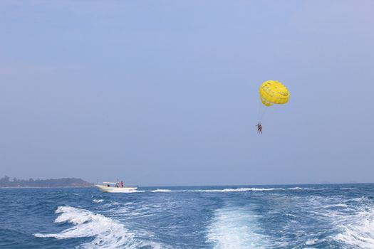 two of young people playing parashoot umbrella by boat pulling in sea water