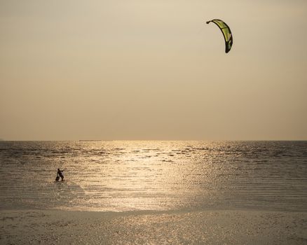 man with kite surving standing in sea water against evening sun light composition by minimalist style