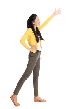 Full length Asian woman hand raised reaching or grabbing something, standing isolated on white background.