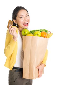 Happy young Asian woman shopper, hands holding shopping bags full of groceries and showing credit card, isolated standing on white background.