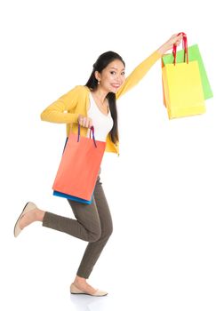 Happy young Asian woman shopper running, hands outstretched holding shopping bags and smiling, full length isolated standing on white background.