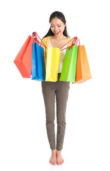 Happy young Asian female shopper, hands holding shopping bags and smiling, full length isolated standing on white background.