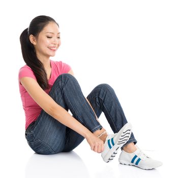Portrait of young Asian woman in pink shirt and jeans wearing sneakers, full body seated isolated on white background.