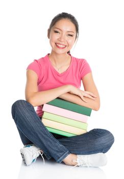 Full body young Asian university female student in pink shirt with stack of textbooks, seated on floor, full length isolated on white background.