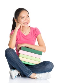 Full body young Asian college female student in pink shirt with stack of textbooks, seated on floor, full length isolated on white background.