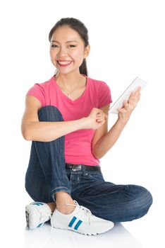 Full body young Asian girl in pink shirt using digital tablet computer, seated on floor, full length isolated on white background.