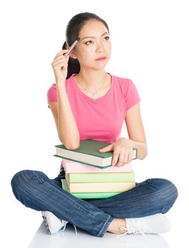 Full body young Asian female student in pink shirt with textbooks, seated on floor, full length isolated on white background.