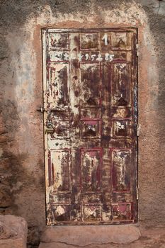 Wooden door with a very worn painting, the same as the wall around. Various numbers written on the door. Photo taken in Morocco.